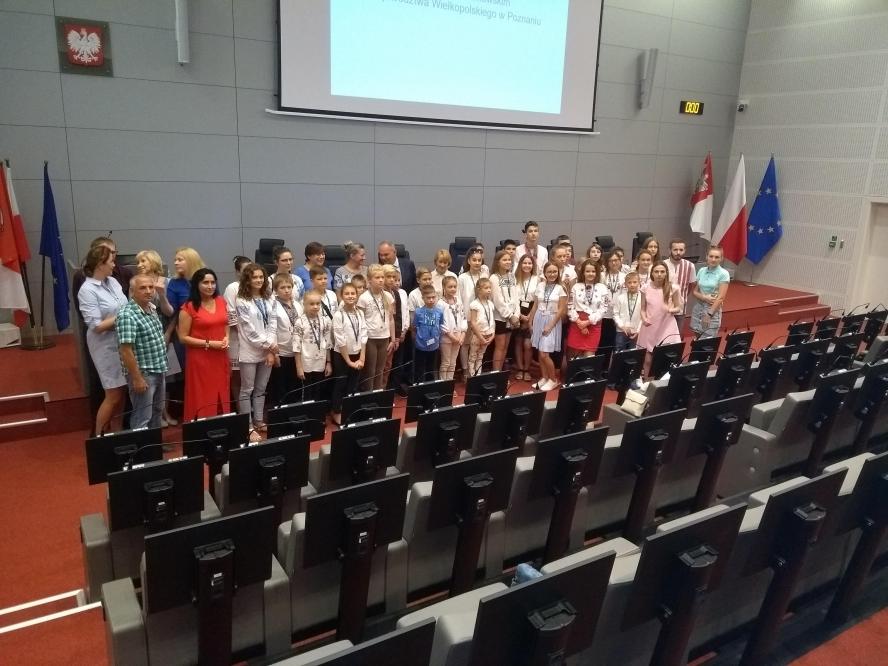 Młodzież na tle prezydium Sejmiku Województwa Wielkopolskiego w Sali Sesyjnej- kliknij aby powiększyć