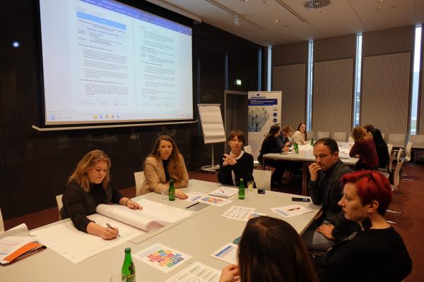 zbliżenie na jedną z grup roboczych, na ekranie wyświetlony dokument agendy, uczestnicy dyskutują i notują na dużych arkuszach- kliknij aby powiększyć