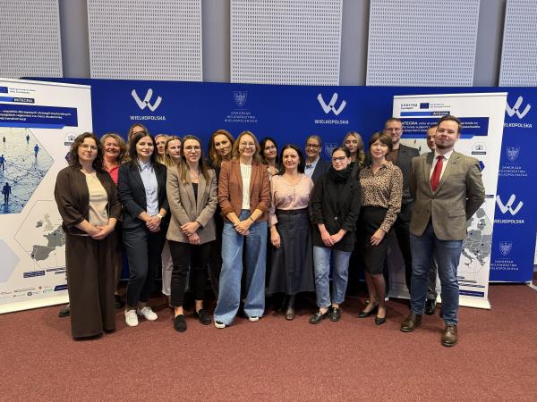 Grupa osób stojących w dwóch rzędach pozuje do wspólnego zdjęcia w sali konferencyjnej na tle niebieskich ścianek i banerów z logo projektu INTEGRA oraz Województwa Wielkopolskiego- kliknij aby powiększyć